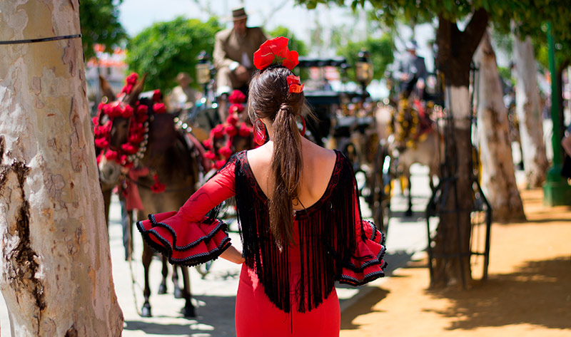 Mujer vestida de gitana en la Feria de Abril con un vestido rojo y negro y una flor en el pelo