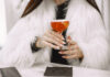 Una chica con un abrigo de pelo blanco sujetando un cocktail cosmopolitan