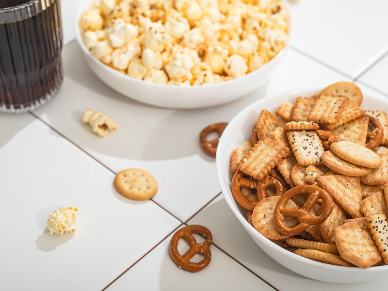 Homemade goodies, fast food - a bowl with popcorn, crackers and cookies on a white table. Fast food is not useful for relaxation