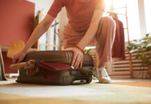 Close-up of woman closing her suitcase with clothes preparing for journey
